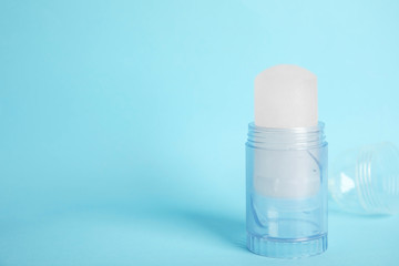 Natural crystal alum stick deodorant and cap on light blue background. Space for text