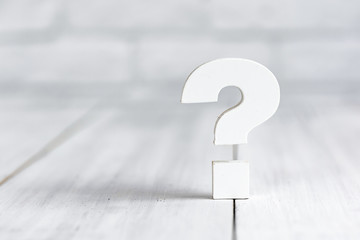 Question mark on white wood table over white brick background with copy space.