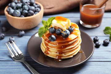 Delicious pancakes with fresh blueberries, butter and syrup on blue wooden table