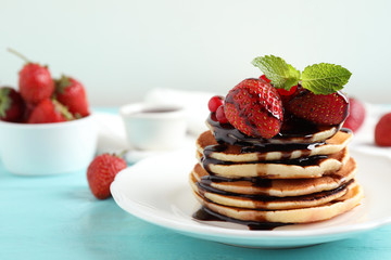 Delicious pancakes with fresh strawberries and chocolate syrup on light blue wooden table
