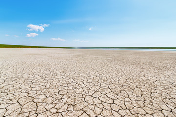 The surface of the cracked dry ground with the tiny stripe of the water and green grasses on the horizon. Gruzskoe lake, Rostov-on-Don region, Russia
