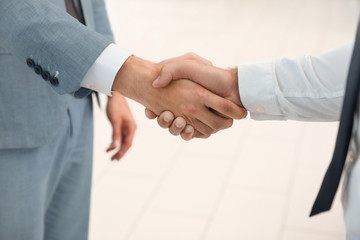 Young salesman shaking hands with client in modern car dealership, closeup