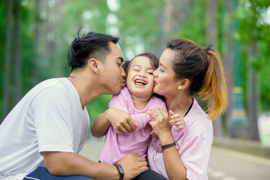Young parents kissing their daughter in the park