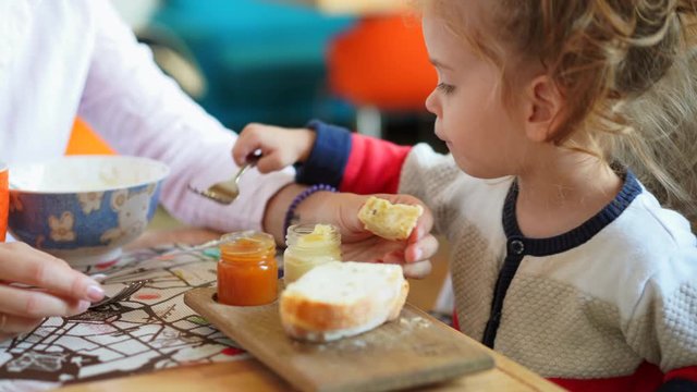 Little Caucasian girl, child, eating delicious bread and jam at a table in a cafe with her mother. Healthy and nutritious breakfast