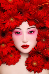 Vintage style portrait of beautiful asian girl with fancy makeup and red flowers around face
