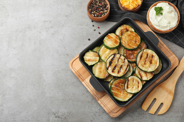 Flat lay composition with delicious grilled zucchini slices on grey table. Space for text