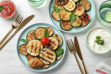 Flat lay composition with delicious grilled zucchini slices on white wooden table