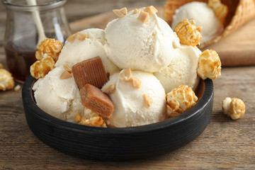 Plate of delicious ice cream with caramel candies and popcorn on wooden table, closeup