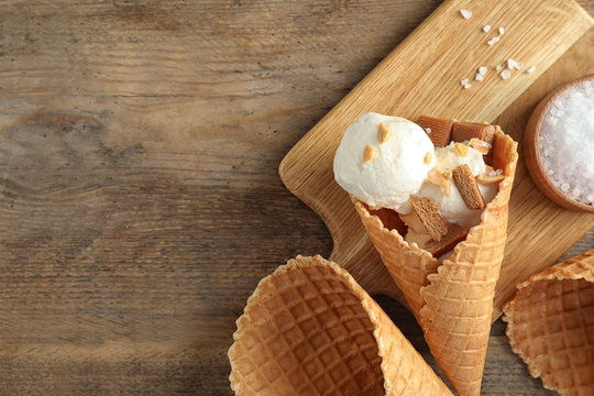 Waffle Cone With Ice Cream, Caramel And Nuts On Wooden Table, Top View. Space For Text