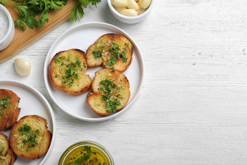 Slices of toasted bread with garlic and herb on white wooden table, flat lay. Space for text