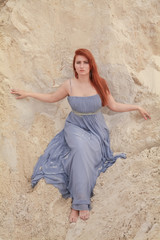 Young beautiful Caucasian woman in evening shiffon dress posing in desert landscape with sand.