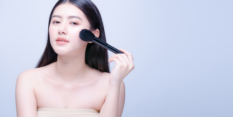 Beauty Asian Woman with Makeup Brushes. She smiling and looking camera to powder brush, Natural makeup with beautiful v-shape face and long hair style.