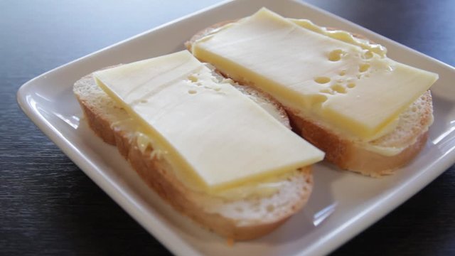2 white bread sandwiches with butter and cheese on a plate. the camera moves around this to the right. close-up