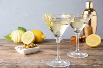 Glasses of lemon drop martini cocktail with zest on wooden table against grey background