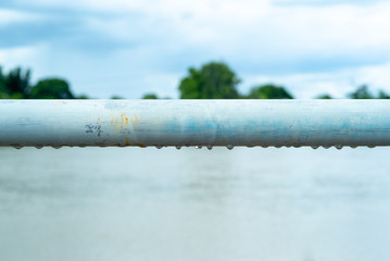 Selective focus on raindrops hanging under steel bar.