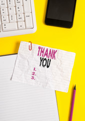 Text sign showing Thank You. Business photo text a polite expression used when acknowledging a gift or service Crumpled white paper on table with paper clips clock mobile and pc keyboard