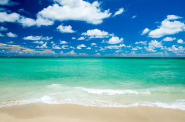 Bright scenic view of tropical Caribbean waves lapping the golden sands of a sunny beach under...