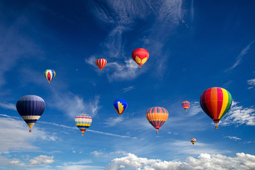 Colourful hot air balloons flying over white clouds and blue sky.