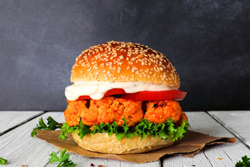 Cauliflower burger with buffalo sauce against a dark background. Healthy eating, plant based meat...