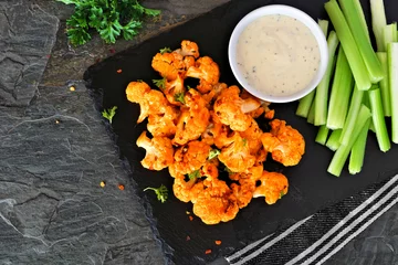 Tuinposter Cauliflower buffalo wings with celery and ranch dip. Top view with a dark slate background. Healthy eating, plant based meat substitute concept. © Jenifoto
