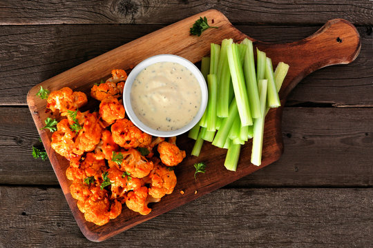 Cauliflower buffalo wings with celery and ranch dip. Top view on a wood paddle board. Healthy eating, plant based meat substitute concept.