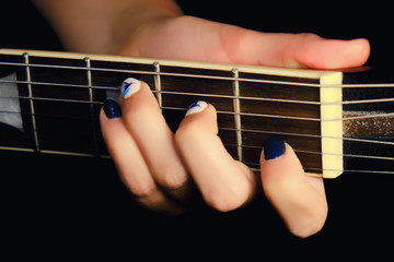 Fototapeta na wymiar Female hand with manicure lying on the wooden neck of the guitar. Woman guitarist clamped a chord on the strings of the musical instrument.