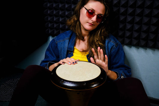 A young woman plays a drum djembe sitting on the floor in a recording Studio. Ethnic African percussion instrument Darbuka.