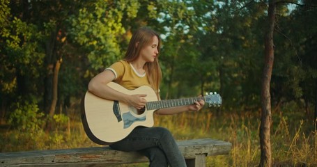 beutiful young woman in yellow shirt on nature background in forest sitting ,  playing on her guitar and smiling , look at the camera with emotions - Powered by Adobe