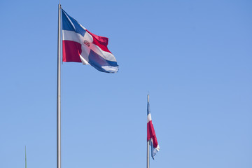 Two Flag of Dominican Republic (DR) waving in the wind with blue sky on background