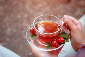 Fruit red tea with wild berries in glass cup, in forest, on bright background.