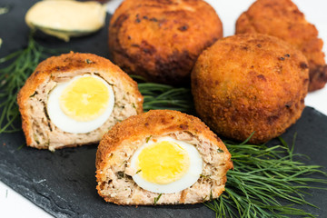 Scotch eggs made with tuna fish and quail eggs on black plate.