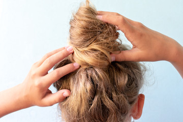 The girl straightens the disheveled bun on her head with her hands. Modern fast hairstyle. Blue background. Blond curly hair.