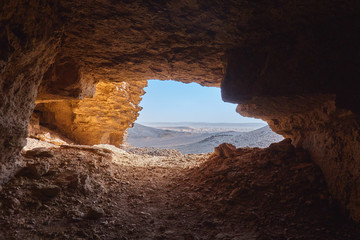 View from the inside of a cave to the rocky desert in the Sahara in Sudan lying under a glistening sun. - Powered by Adobe