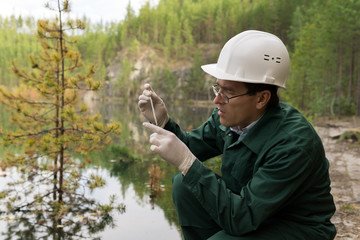industrial ecologist takes a sample of water from a flooded quarry - obrazy, fototapety, plakaty