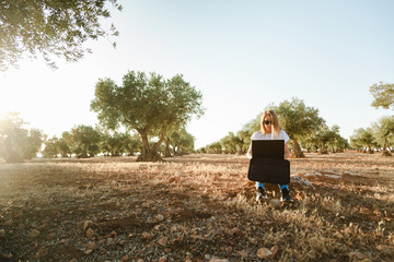Fototapeta premium Young woman with a laptop case seated in the olive tree field