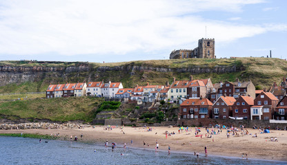 Whitby, North Yorkshire, England - Aug 24, 2019:,UK.The harbour at Whitby on Yorkshire coast,View of people bathing in the sun, swimming and playing on the beach,Tourists on the sand beach in summer