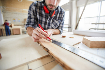 Closeup of unrecognizable carpenter measuring wood while working in joinery shop, copy space