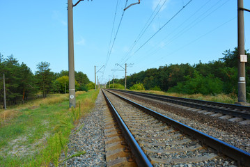 Fototapeta na wymiar Railway track, railway and electric power lines for electric vehicles, electric trains lying along coniferous forests with blue sky, clouds. Infrastructure of Severny housing estate, Dnipro, Ukraine.