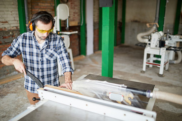 High angle portrait of mature carpenter cutting wood in joinery workshop, copy space