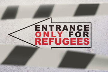 An arrow-shaped sign on the wall with the words "Entrance only for refugees" behind a striped obstruction tape