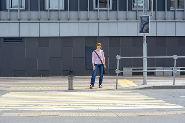 Red-haired casual dressed middle-aged woman with freckles is waiting at a pedestrian crossing.