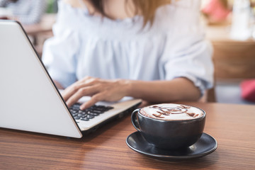 Young woman using smart phone and laptop with cup of coffee in cafe