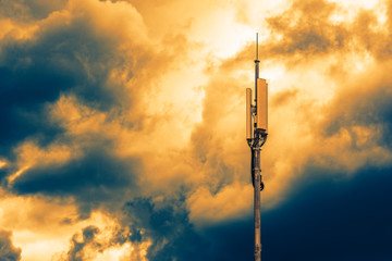 A column with transmitters and mobile telephony antennas against the sky with clouds at sunrise