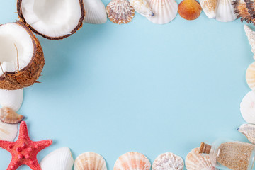 Flat lay frame composition with beautiful starfishes, sea shells, coconut and bottle with sand on a blue background, space for text. Copy space