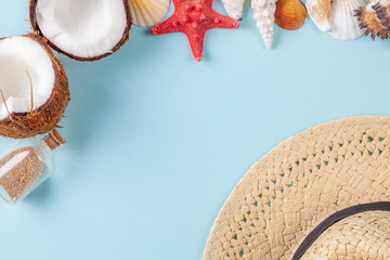 Flat lay composition with beautiful starfishes, sea shells, coconut, straw hat and bottle with sand on a blue background, space for text. Copy space