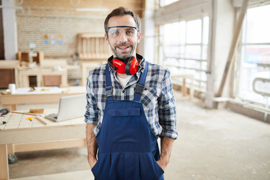 Waist up portrait of smiling mature carpenter looking at camera while posing in workshop, copy space