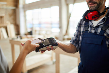 Closeup of unrecognizable customer paying via NFC in joinery shop, copy space