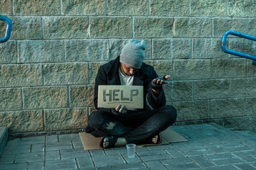 A man, homeless, a person asks for alms on the street with a Help sign. Concept of homeless person, addict, poverty, despair.