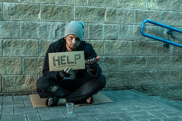 A man, homeless, a person asks for alms on the street with a Help sign. Concept of homeless person, addict, poverty, despair.