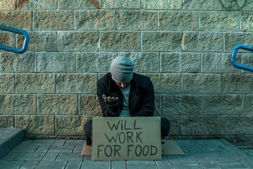 A man, homeless, a man asks for alms on the street with a sign will work for food. Concept of...